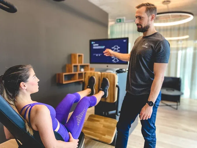 Two trainers consulting with client in bright, minimalist gym space showcasing personalized coaching approach.